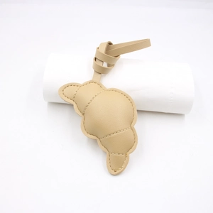 Dettaglio del ciondolo in pelle beige a forma di croissant con trama a grana e cuciture
