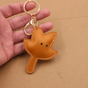 Detailed view of handmade maple leaf leather keychain with gold hardware and white stitching