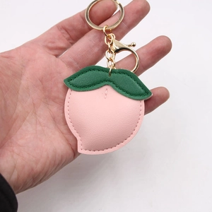 Pink faux leather peach keychain with green leaf and golden metal ring on white background