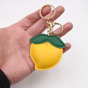 Handheld photo of a yellow lemon-shaped leather keychain with golden metal ring and clasp