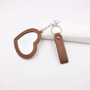 Détail d'un miroir de poche en forme de cœur en cuir marron avec porte-clés en métal argenté