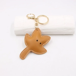 Detail view of brown leather leaf keychain with fine white stitching and gold hardware