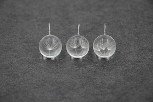 Vue macro de trois pendentifs en verre avec de vrais pissenlits séchés sur feutre gris