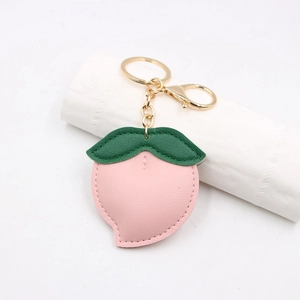 Close-up of pink leather peach keychain with green leaf and golden metal clasp