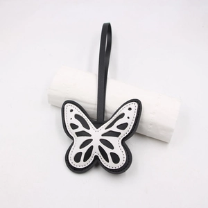 Detail of laser-cut hollow butterfly leather bag charm with white stitching and black lanyard