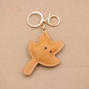 Detailed view of handmade maple leaf leather keychain with caramel finish and white stitching