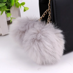 Dual grey faux rabbit fur pompoms with golden chain keychain on a black leather bag