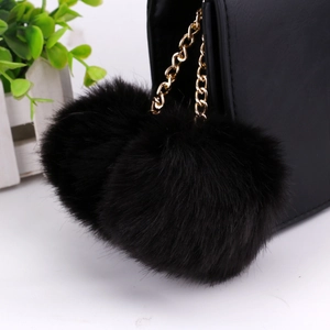 Detail of soft black faux rabbit fur double pom pom keychain with gold chain on a bag