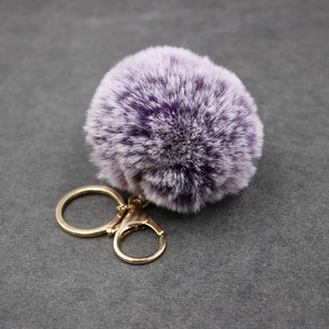 Plush faux rabbit fur keychain in gradient purple with gold metal clasp on stone background