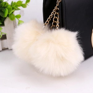 Detail of soft cream-white faux fur poms with gold chain on a black leather bag