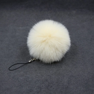 Detail of soft cream faux fur pompom keychain with a black braided cord attachment