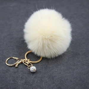Detail of cream faux fur keychain with golden clasp and colorful rhinestone ball