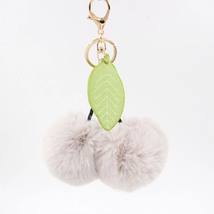 Détail d'un porte-clés cerise en fausse fourrure rose avec feuilles en cuir vert et fermoir doré