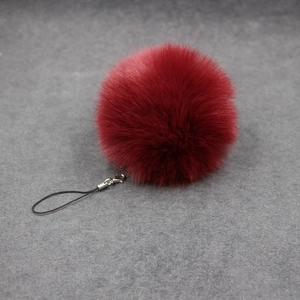 Detailed view of fluffy burgundy faux rabbit fur pompom with silver clasp and black cord