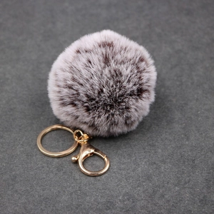 Detailed macro view of dual-tone grey faux fur pompom with golden metal lobster clasp