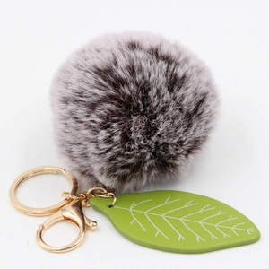 Close-up of fluffy faux rabbit fur ball keychain with green leaf and gold metal ring