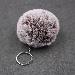 Close-up of soft purple-grey faux rabbit fur pompom keychain with brown spotted texture
