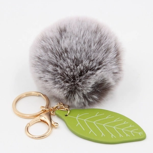 Detail of soft grey faux fur pompom keychain with green leaf charm and golden metal hardware