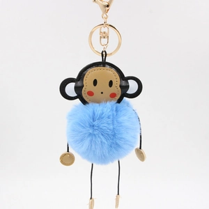 Close-up of blue plush monkey keychain with fluffy fur ball and gold lobster clasp