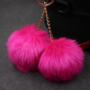 Detail view of fuchsia faux rabbit fur double pompom keychain on a black textured bag