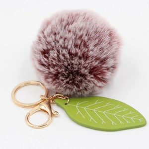 Macro view of gradient burgundy faux fur pompom and green leaf charm with gold hardware
