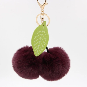Détail du porte-clés cerise en peluche avec pompons violet foncé et feuille en cuir vert