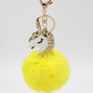 Close-up of fluffy yellow pompom unicorn keychain with gold sequins and metal clasp