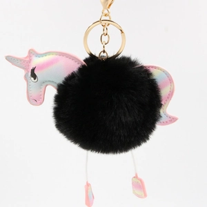 Detail of colorful unicorn keychain with large black fluffy pom pom and gold metal clasp