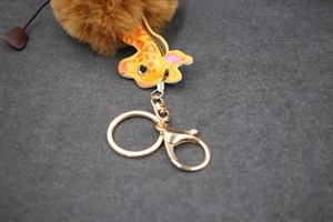 Close-up of giraffe plush keychain with golden lobster clasp and brown pompom detail