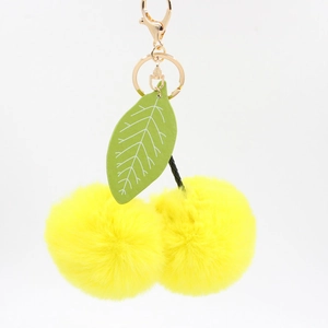 Détail de porte-clés cerise en pompon jaune avec feuille verte et fermoir en métal doré