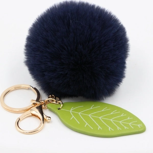 Detail of navy blue faux fur pompom keychain with green leaf charm and gold hardware