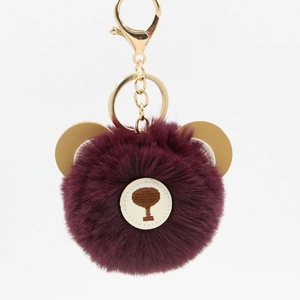 Detailed macro view of the fluffy burgundy faux fur bear keychain with golden hardware