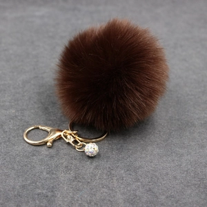Detail of a fluffy brown fur pompom keychain with golden clasp and rhinestone ball charm