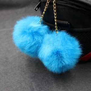 Detail of bright blue fluffy double pom-pom charms with gold chain on a black handbag