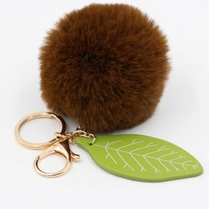Detail of soft brown faux fur pom pom and green leaf pendant on gold keychain