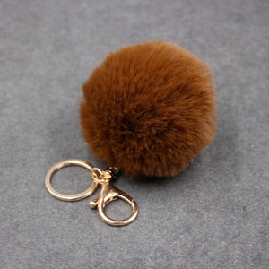 Vue détaillée d'un pompon en fausse fourrure marron avec mousqueton et anneau dorés