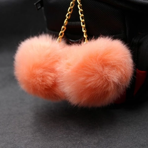 Detail of soft coral orange double faux fur pompom charm on a black backpack