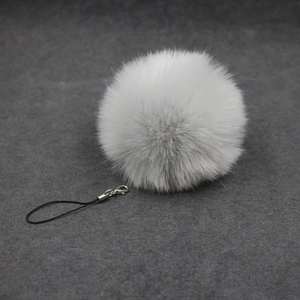 Close-up of fluffy white faux fur pom-pom charm with silver lobster clasp and strap