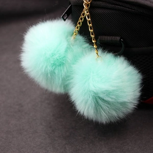 Detail of two mint green fluffy faux rabbit fur balls with gold metal chain on bag