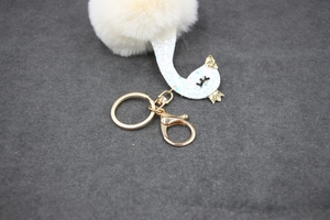Detail showing white swan plush keychain with sparkling crown and golden metal hardware