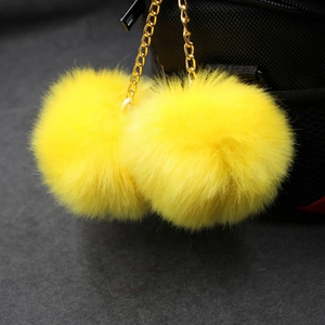 Detailed view of yellow faux fur double balls on golden chain attached to a black bag