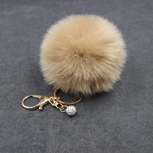 Macro shot of fluffy khaki faux fur pompom keychain with golden clasp and crystal ball