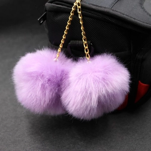 Detailed view of dual purple faux fur pompom bag charms with golden chain links
