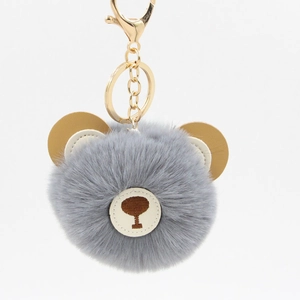 Detail of grey fluffy bear keychain with faux fur pompom and golden metal ring and clasp