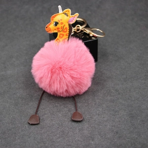 Detailed shot of pink plush ball keychain with an orange leather giraffe charm and gold clasp