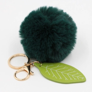 Detail of dark green faux rabbit fur pom pom with gold metal keyring and leather leaf