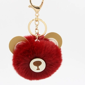 Close-up of fluffy dark red bear pompom keychain with golden metal hook and embroidery