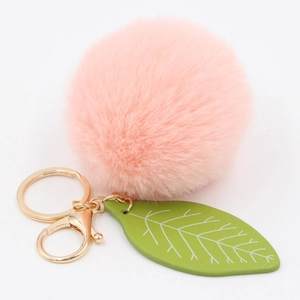 Detail of pink faux rabbit fur ball keychain with green leaf charm and golden metal clasp