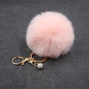 Detail of pink faux fur pompom keychain with golden lobster clasp and rhinestone ball charm