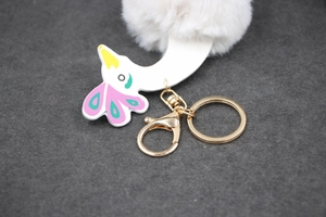 Détail d'un porte-clés pompon blanc avec breloque d'oiseau et métal doré sur feutre